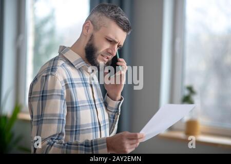 Smart young man with smartphone and sheet of paper. Stock Photo