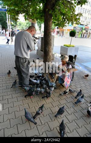 Sofia, Bulgaria - June 16, 2018: Unidentified old woman and man on pavement in midst crowd of doves to feed and kiss them Stock Photo