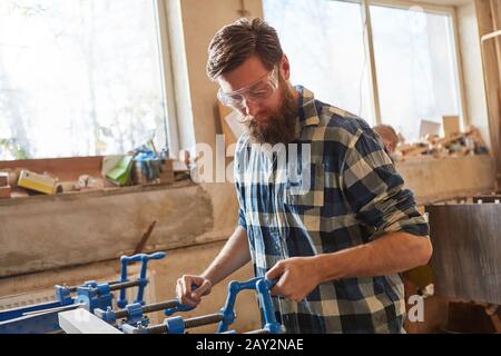 Carpenter with safety glasses as a furniture maker works with wood on a vice Stock Photo