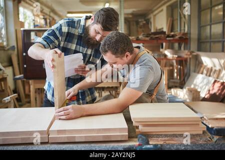Two furniture builders measuring furniture part for a shelf in the carpentry Stock Photo
