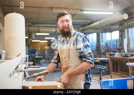 Carpenter apprentice works as a furniture maker with wood on the grinding machine Stock Photo
