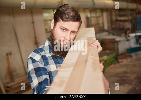 Hipster man as a carpenter apprentice carries a board as lumber in the joinery Stock Photo