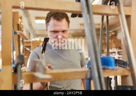 Carpenter apprentice works with screw clamps in the carpentry of furniture making Stock Photo