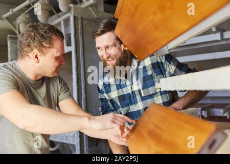 Two carpenters as furniture makers discuss a wooden workpiece in the joinery Stock Photo