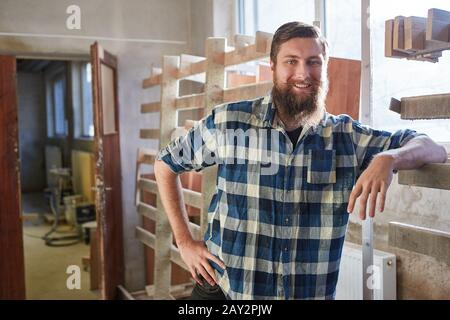 Smiling man with beard as a hipster carpenter in the carpentry workshop Stock Photo