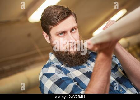 Hipster carpenter with a beard in a carpentry workshop carries a wood board Stock Photo
