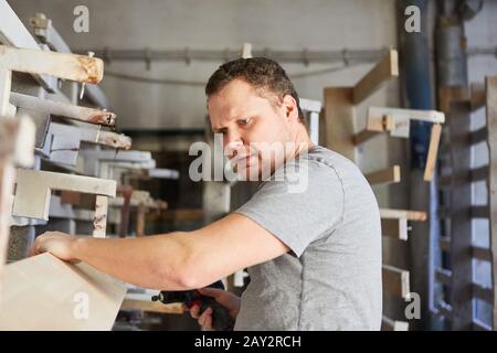 Young carpenter checks quality of wood plank in warehouse in carpentry Stock Photo