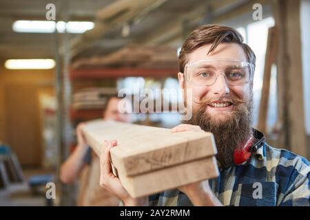 Hipster with a beard as a carpenter apprentice carries wooden beams in the carpentry workshop Stock Photo
