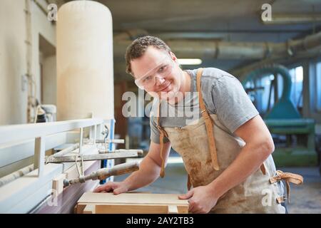 Carpenter with safety glasses works on the grinding machine with a wooden workpiece Stock Photo