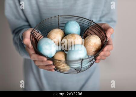 Hands holding colored eggs in wire basket Stock Photo