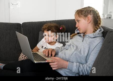 Sisters on sofa using laptop Stock Photo