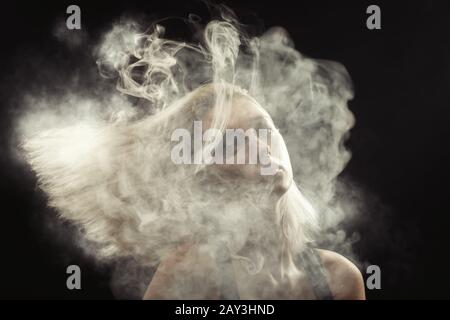 young blond woman dancing at white smoke cloud on black background Stock Photo
