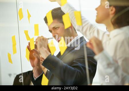 Business team writes notes while brainstorming on a glass wall Stock Photo