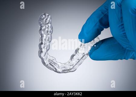 Close-up Of Dentist  Hand Holding Transparent Plastic Braces Over Gray Backdrop Stock Photo