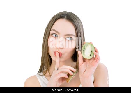 Beauty portrait of a pretty smiling woman with healthy skin showing silence gesture with finger over her lips and holding kiwi slices, isolated over l Stock Photo