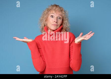 Quizzically attractive senior female in red sweater on blue background. Mother does not know right solution. studio shot Stock Photo