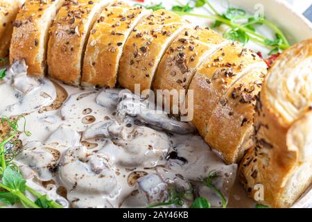 Puff pastry roll stuffed with mushrooms. Nearby are champignons in sour cream, sliced. Served with microgreen and sun-dried tomatoes. On a dark backgr Stock Photo