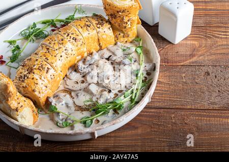 Puff pastry roll stuffed with mushrooms. Nearby are champignons in sour cream, sliced. Served with microgreen and sun-dried tomatoes. On a dark backgr Stock Photo