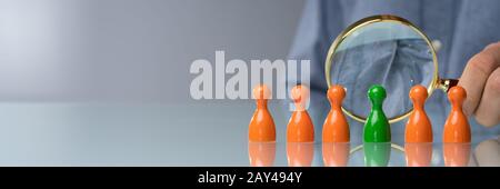 Businessperson's Hand Holding Magnifying Glass Over Green Pawn On Desk Stock Photo