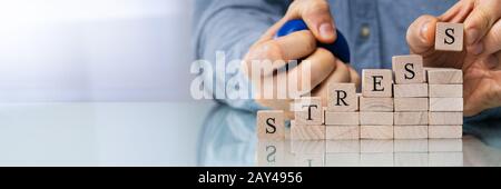 Close-up Of Person's Hand Placing Last Alphabet Of Word Stress On Wooden Block Stock Photo