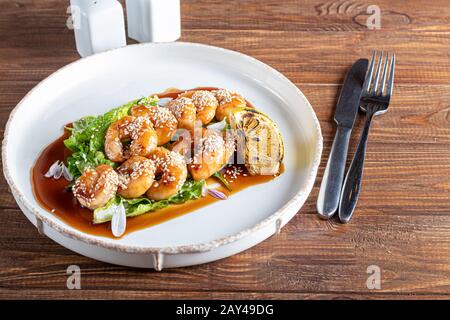 Shrimps cooked in teriyaki sauce with a slice of fried lemon on a pillow of lettuce leaves. On a white background, on a dark wooden background. Copy s Stock Photo