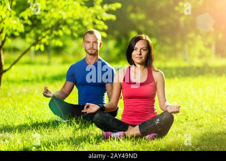 Young man and woman doing yoga in the sunny summer park Stock Photo