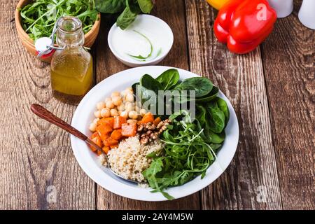 Preparing fresh salad with chickpeas, spinach, arugula, quinoa, carrot, walnuts. Greek yogurt and homemade salad dressing, vegetables, herbs on rustic Stock Photo