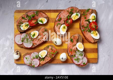 Bagels with boiled quail eggs and smoked salmon on rustic wooden background, top view Stock Photo