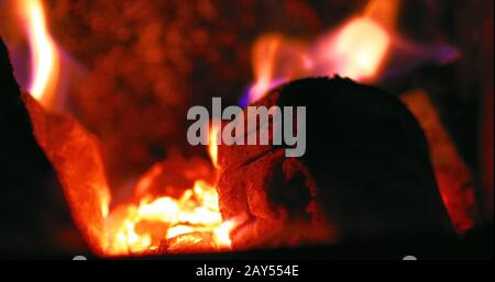 burning red fire and smoldering charcoal close-up, fire flame abstract sparkle black and orange smoke background, selective focus, cracks Stock Photo