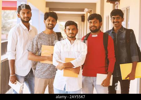 Happy young students holding books and standing at college corridor - Group of multiracial confident youth at university campus - concept of Stock Photo