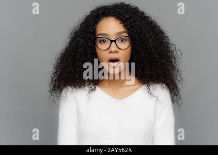 Candid shot of shocked beautiful woman in glasses with dark frizzy hair, keeps jaw dropped from amazement, being in stupor after finding out something Stock Photo