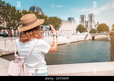 Happy traveler girl blogger takes photos of Notre Dame De Paris and the river Seine for her social media Stock Photo