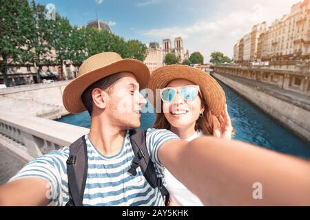 Couple of friends taking selfie photo from a bridge over Seine river with Notre Dame Cathedral on the background Stock Photo
