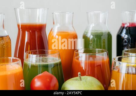 Close up shot of glass bottles filled with colorful juice made of various vegetables and fruit, red tomato and green apple in foreground. Fresh detox Stock Photo