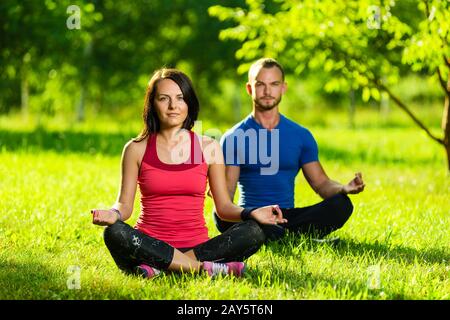 Young man and woman doing yoga in the sunny summer park Stock Photo