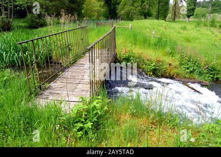 Wooden and iron footbridge on a course of eau dans a country landscape. Stock Photo