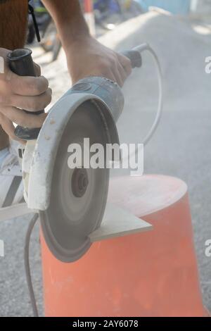 Skilled worker cuts tiles with angle grinder under dust exposure Stock Photo
