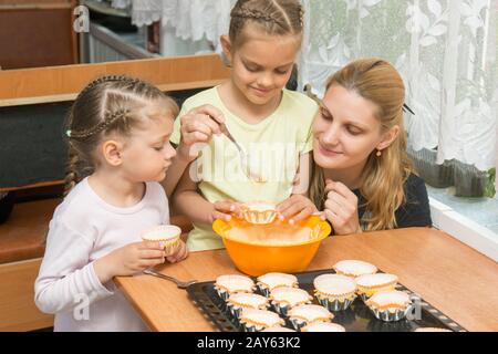 The elder daughter pours batter for cakes in tins, under the care of my mother and younger sister Stock Photo