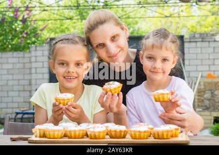 Mother and two daughters sitting at the table with Easter cupcakes in his hands and looked into the frame Stock Photo