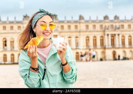 Asian woman eating croissant and drinking a cup of coffee while resting in Versailles. Travel and french cuisine concept Stock Photo