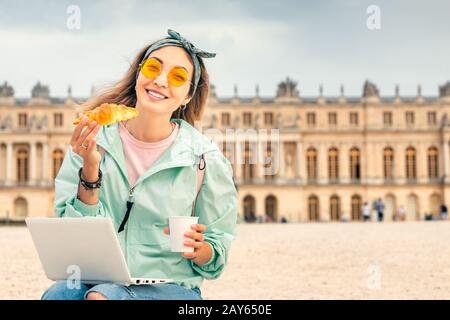 Asian woman eating croissant and drinking a cup of coffee while resting in Versailles. Travel and french cuisine concept Stock Photo