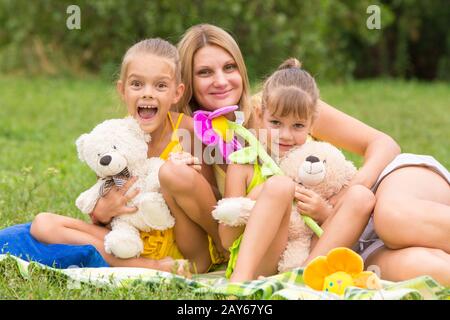 Mother and two daughters sitting with soft toys on a picnic Stock Photo
