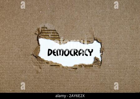 The word democracy appearing behind torn paper Stock Photo