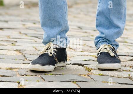 Feet dressed in blue jeans and sneakers man closeup on stone pavement Stock Photo