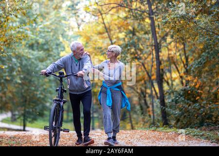 Mature couple woman and man with bicycle walking in the park and talk Stock Photo