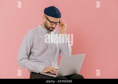 Caucasian male copywriter dressed in stylish clothes, works freelance, types information on laptop computer, connected to wireless internet, has atten Stock Photo