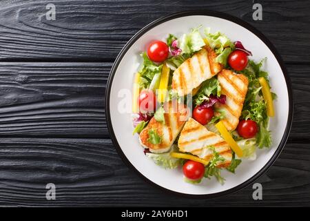 Cheese salad with grilled halloumi with fresh vegetables close-up on the plate on the table. Horizontal top view from above Stock Photo