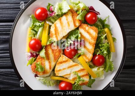 Grilled halloumi cheese served with fresh vegetables close-up in a plate on the table. Horizontal top view from above Stock Photo