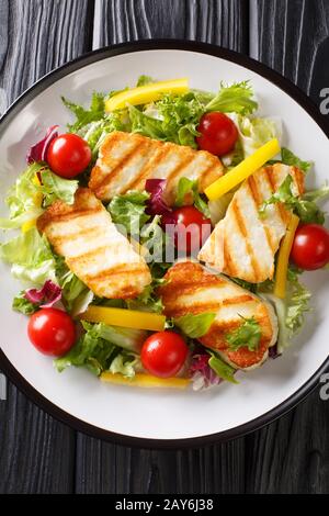 Fresh salad with grilled halloumi cheese with vegetables closeup at the plate on the table. Vertical top view from above Stock Photo