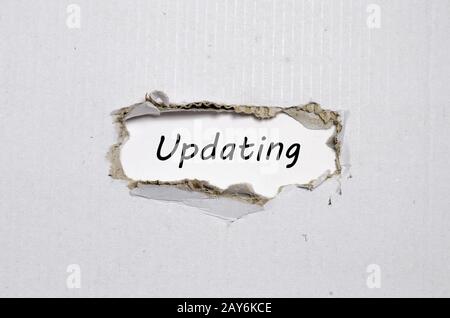 The word updating appearing behind torn paper Stock Photo